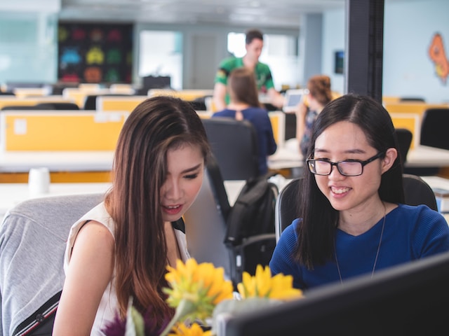 Two women smiling in front of computer monitor