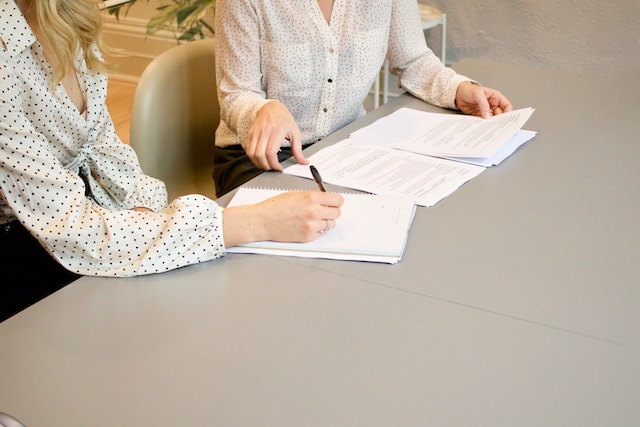 Woman signing on white printer paper beside another woman 